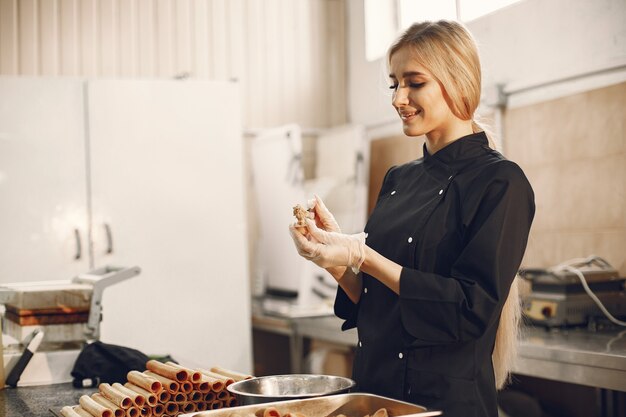 Giovane donna bionda in uniforme nera nella cucina del ristorante che prepara diversi dolci e biscotti.