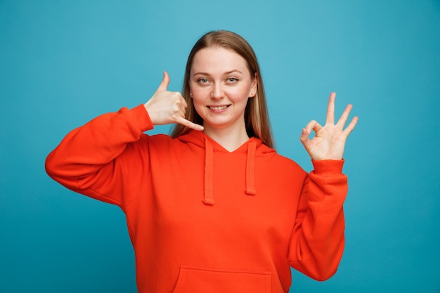 Giovane donna bionda sorridente che fa gesto di chiamata e segno giusto