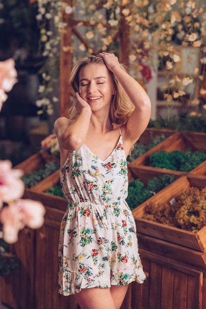 Giovane donna bionda sorridente in vestito floreale che posa al negozio di fiorista
