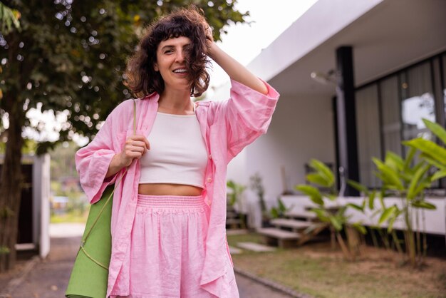 Giovane donna bruna caucasica allegra in abiti casual che sorride alla macchina fotografica mentre si tocca i capelli all'aperto Concetto di stile di vita dell'umore