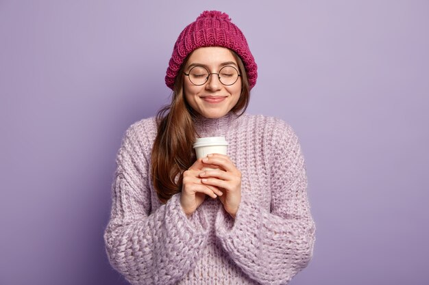 Giovane donna bruna che indossa un maglione viola e tenendo la tazza di caffè