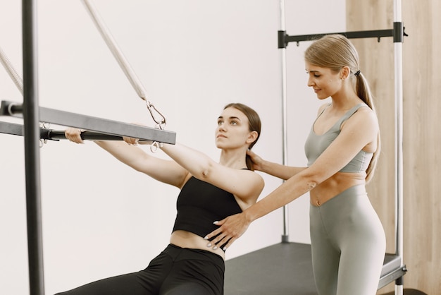 Giovane donna bruna in forma con un allenatore femminile biondo in palestra. Donna che indossa abbigliamento sportivo nero. Ragazza caucasica che allunga con l'attrezzatura.