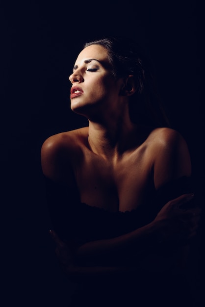 Giovane donna bruna in lingerie nera in illuminazione chiaroscuro.