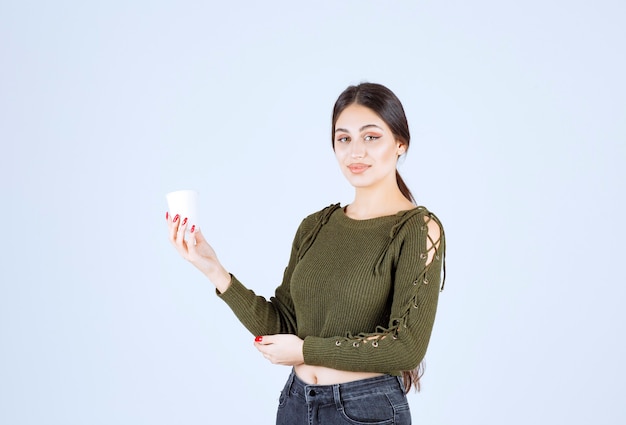 Giovane donna castana che tiene tazza di plastica e posa.