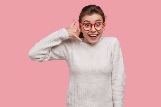 Giovane donna castana in maglione bianco e occhiali rossi
