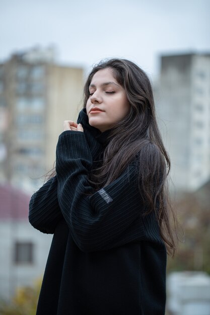 Giovane donna castana in maglione nero in piedi all'aria aperta