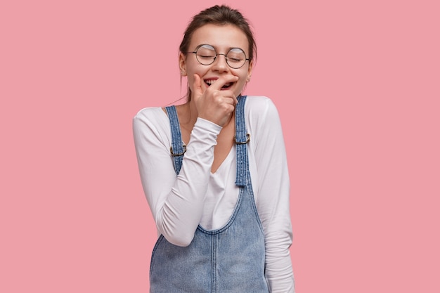 Giovane donna castana in salopette di jeans