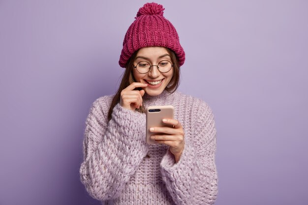 Giovane donna castana in vestiti di inverno accoglienti che tengono telefono