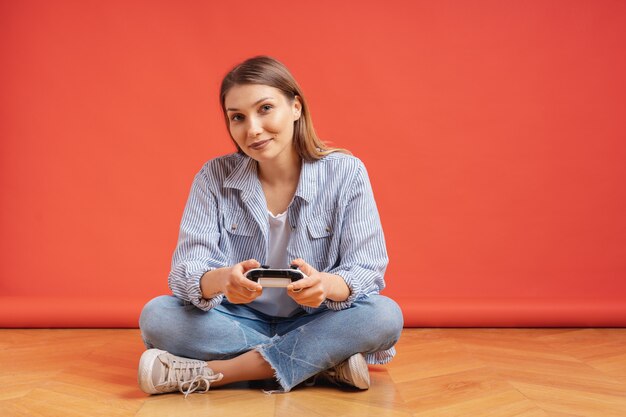 Giovane donna casuale emozionante che gioca i video giochi divertendosi sul rosso