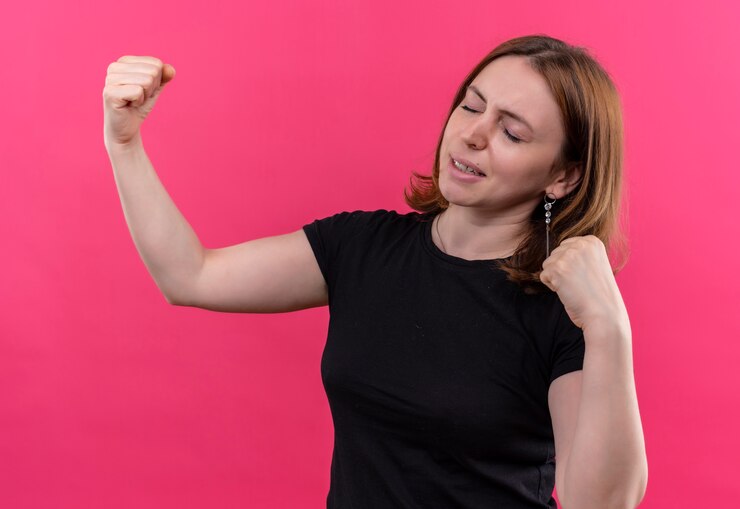 Foto gratuito giovane donna casuale sicura che gesturing forte con i pugni alzati e gli occhi chiusi sullo spazio rosa isolato