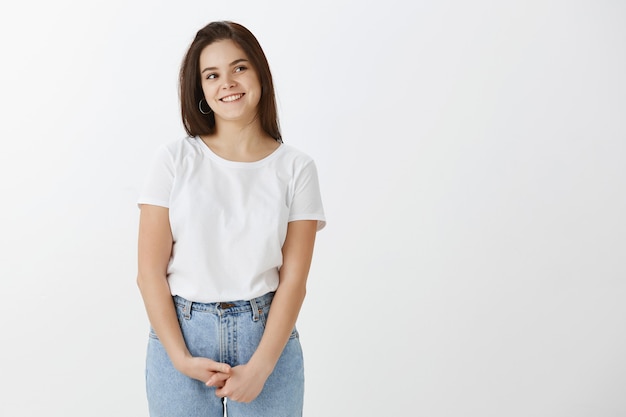 Giovane donna casuale sveglia che posa contro il muro bianco