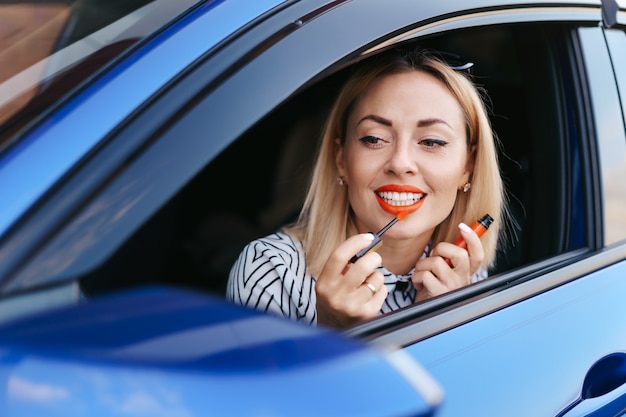 Giovane donna caucasica applicando il rossetto guardando il riflesso nello specchio dell'auto.