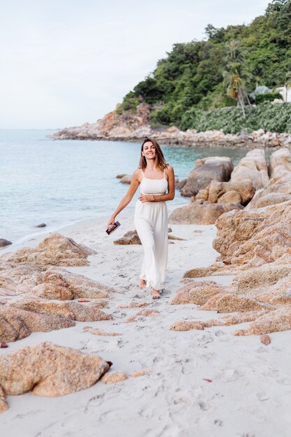 giovane donna caucasica calma felice con ukulele sulla spiaggia rocciosa tropicale al tramonto