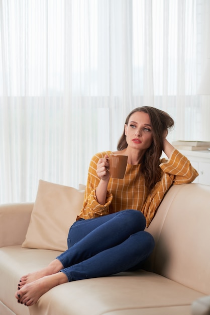 Giovane donna caucasica che si rilassa sullo strato a casa con la tazza