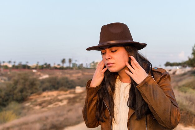 Giovane donna caucasica con un vestito da cowgirl, che si raddrizza i capelli in un ventoso parco naturale