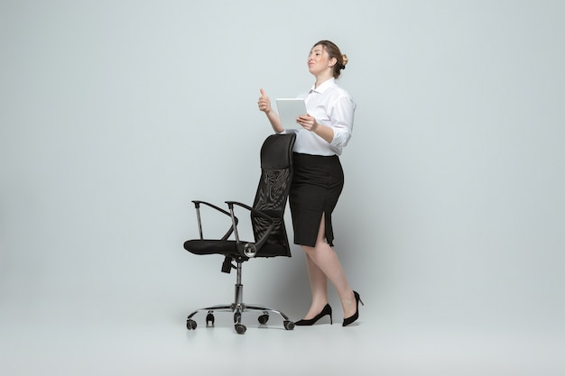 Giovane donna caucasica in abbigliamento casual su grigio. Personaggio femminile bodypositive, taglia forte