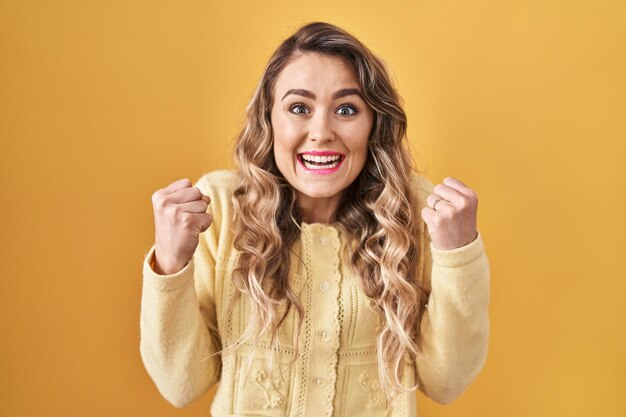 Giovane donna caucasica in piedi su sfondo giallo che celebra sorpreso e stupito per il successo con le braccia alzate e gli occhi aperti. concetto di vincitore.