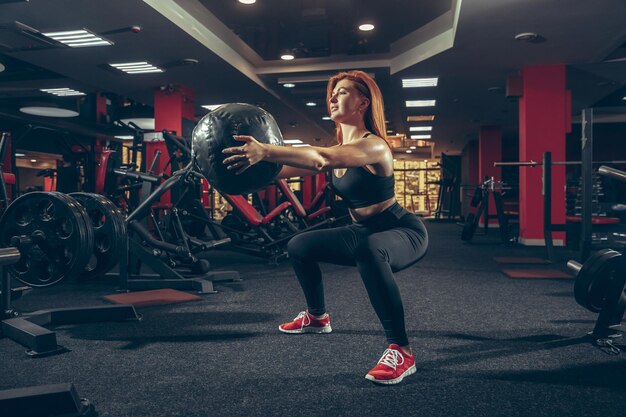 Giovane donna caucasica muscolare che pratica in palestra con attrezzature.