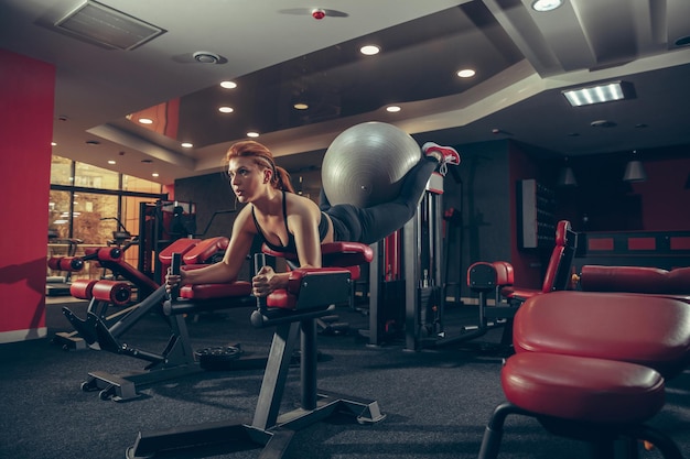 Giovane donna caucasica muscolare che pratica in palestra con attrezzature.