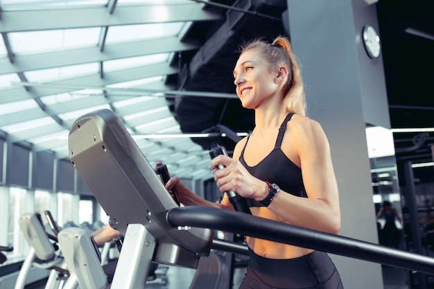 Giovane donna caucasica muscolare praticando in palestra, facendo cardio. Modello femminile atletico facendo esercizi di forza, allenando la parte superiore del corpo. Benessere, stile di vita sano, concetto di bodybuilding.