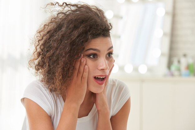 Giovane donna caucasica riccia che posa con il viso e le mani sorpresi sulle guance