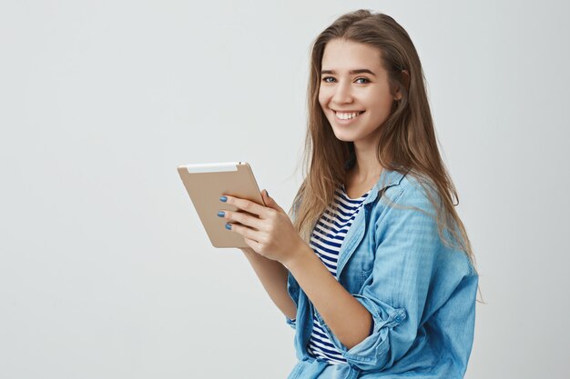 Giovane donna caucasica splendida tenera femminile che indossa i vestiti d'avanguardia che sorride compressa digitale contentissima amichevole amichevole della tenuta