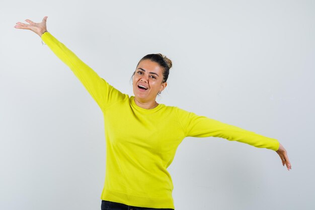 Giovane donna che allarga le braccia in maglione, gonna di jeans e sembra energica