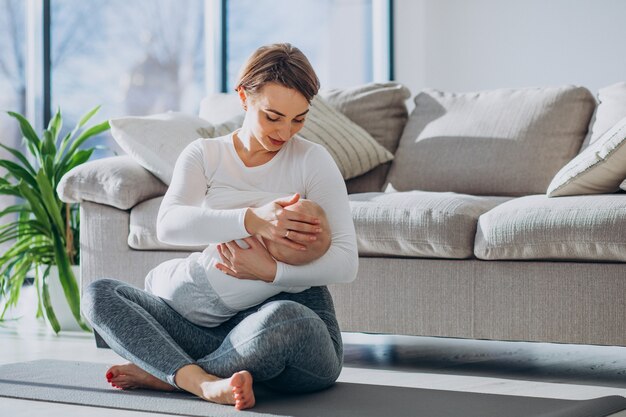 Giovane donna che allatta al seno figlio del bambino e seduto su mat