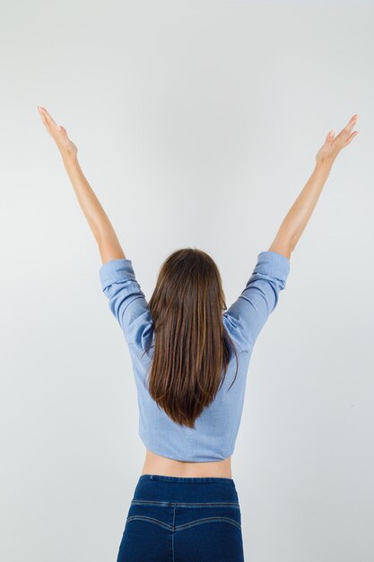 Giovane donna che allunga le braccia in camicia blu, pantaloni e sembra felice