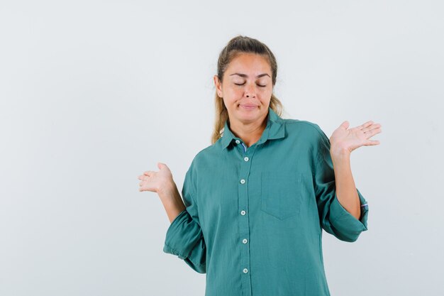 Giovane donna che allunga le mani in modo interrogativo in camicetta verde e guardando pensieroso