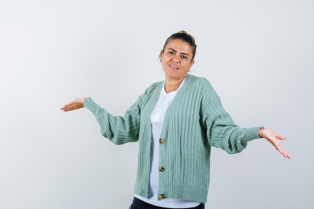 Giovane donna che allunga le mani in modo interrogativo in camicia bianca e cardigan verde menta e sembra felice