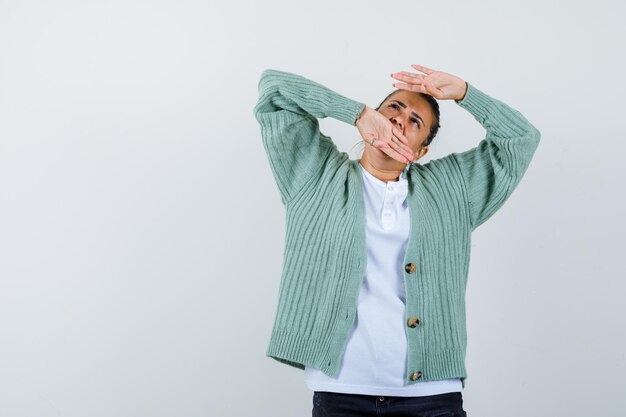 Giovane donna che alza le braccia e guarda sopra in camicia bianca e cardigan verde menta e sembra concentrata