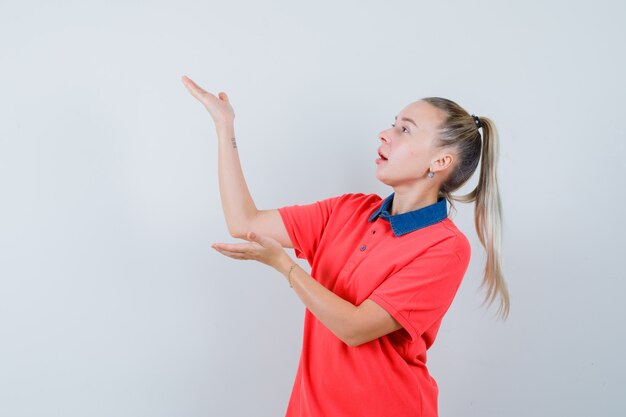 Giovane donna che alza le mani come tenendo qualcosa in t-shirt e guardando concentrato