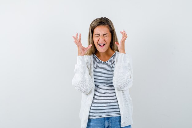 Giovane donna che alza le mani mentre grida in t-shirt, giacca e sembra irritata, vista frontale.