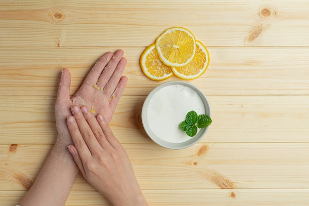 Giovane donna che applica la macchia naturale del limone sulle mani contro il tavolo in legno