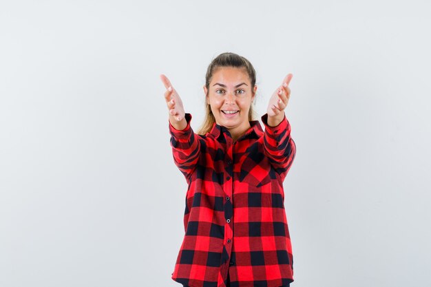 Giovane donna che apre le braccia per abbraccio in camicia casual e sembra allegra, vista frontale.