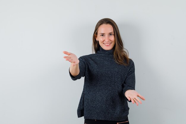 Giovane donna che apre le braccia per abbraccio in camicia e sembra felice. vista frontale.