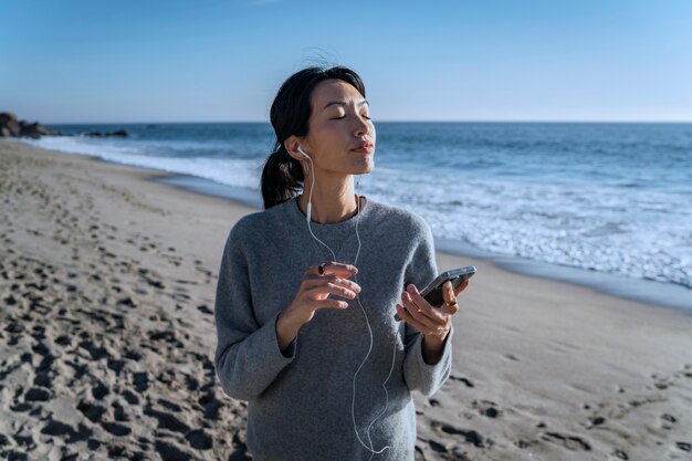 Giovane donna che ascolta la musica sullo smartphone in spiaggia utilizzando gli auricolari