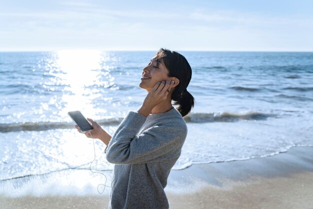 Giovane donna che ascolta la musica sullo smartphone in spiaggia utilizzando gli auricolari