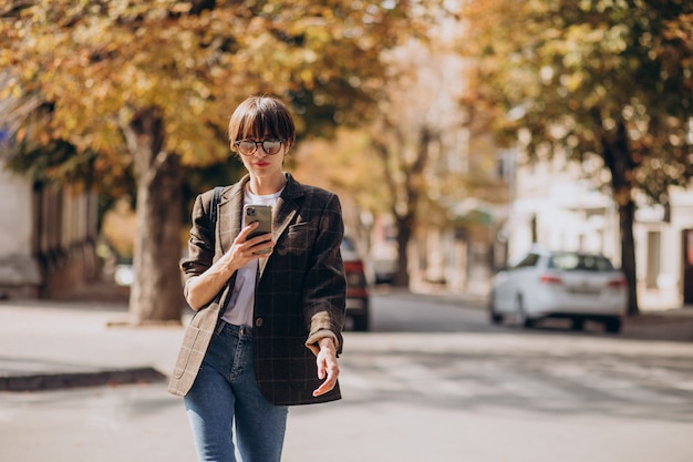 Giovane donna che attraversa la strada e utilizzando il telefono