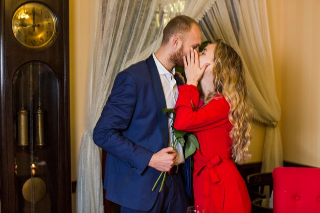 Giovane donna che bacia uomo con fiori sulle labbra