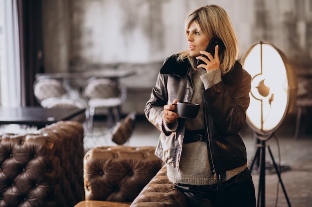 Giovane donna che beve caffè e parla al telefono in un bar