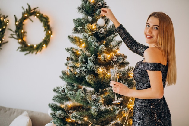 Giovane donna che beve champagne dall'albero di Natale