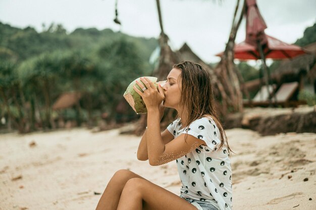 giovane donna che beve cocco tropicale sulla spiaggia