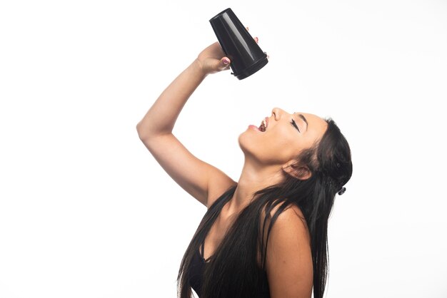 Giovane donna che beve da una tazza sul muro bianco