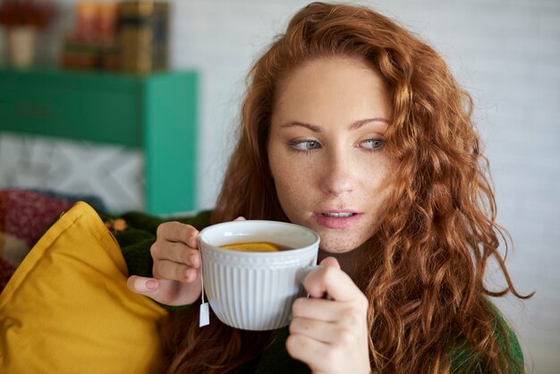 Giovane donna che beve tè al limone in soggiorno