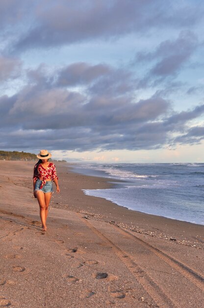 Giovane donna che cammina sulla spiaggia al tramonto