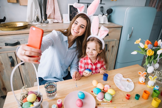 Giovane donna che cattura selfie con la figlia vicino a uova di Pasqua