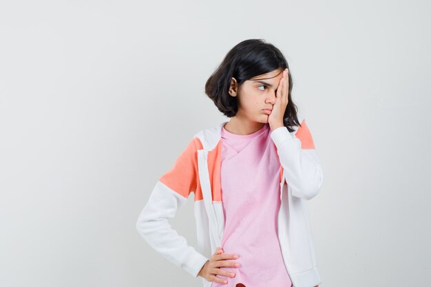 Giovane donna che copre metà del viso con la mano nella giacca, camicia rosa.