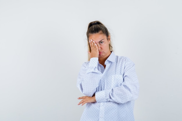 Giovane donna che copre parte del viso con la mano in camicia bianca e sembra stanca